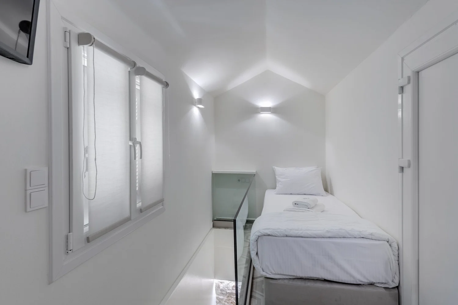 Bedroom three with single bed, white linen and warm wall light
